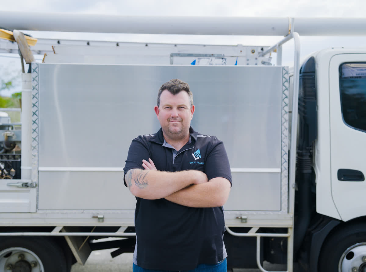 Brent from Westplumb, arms crossed, beside the work truck