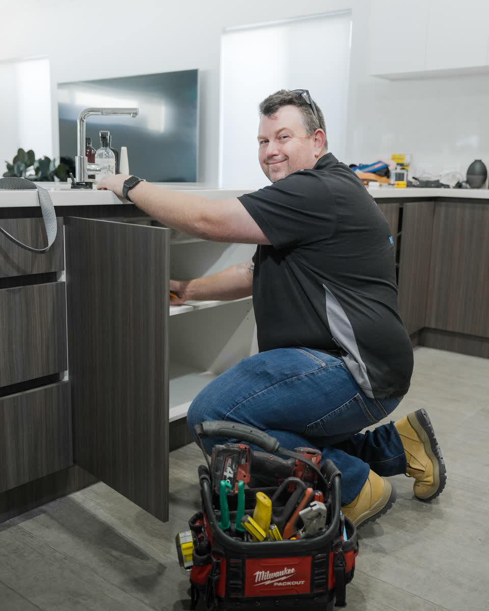 A Westplumb plumber kneeling at a kitchen sink with his tool bag