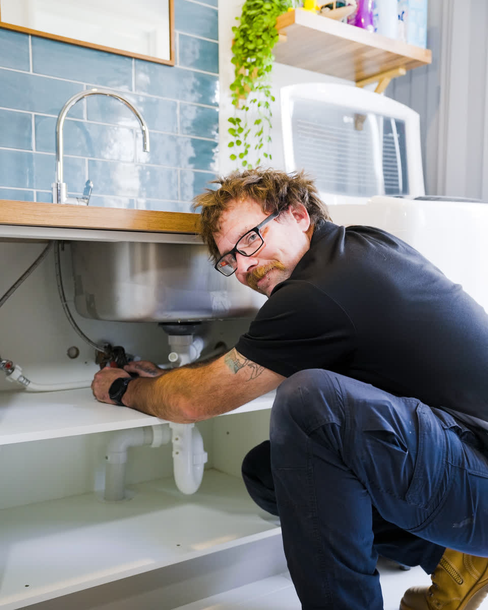 A Westplumb plumber smiling while working under a sink