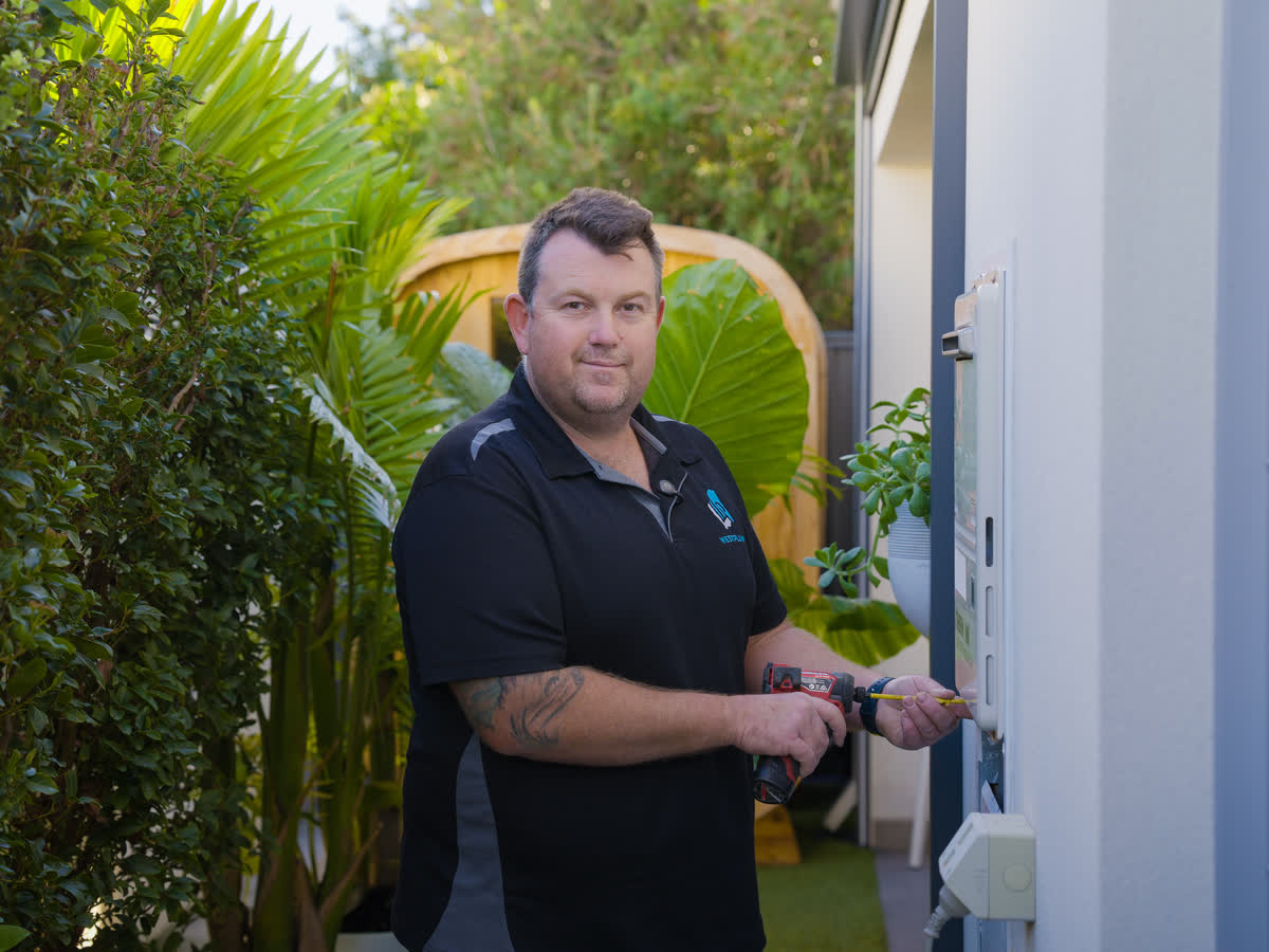 A Westplumb plumber at a continuous flow hot water unit in a garden